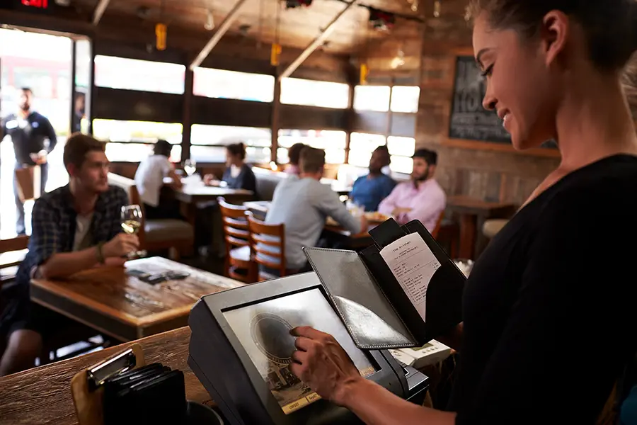 Restaurant owner ringing up customers in a busy dining room — representing small businesses that benefit from local SEO visibility.
