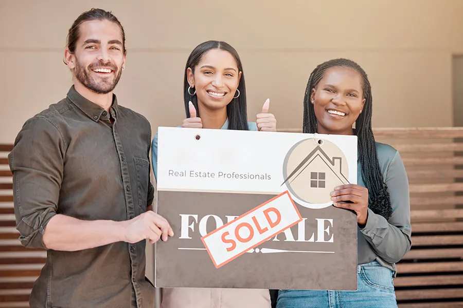 Real estate agent celebrating a successful home closing with a couple holding a SOLD sign — representing how real estate SEO and a user-friendly website can help turn prospective home buyers into clients.