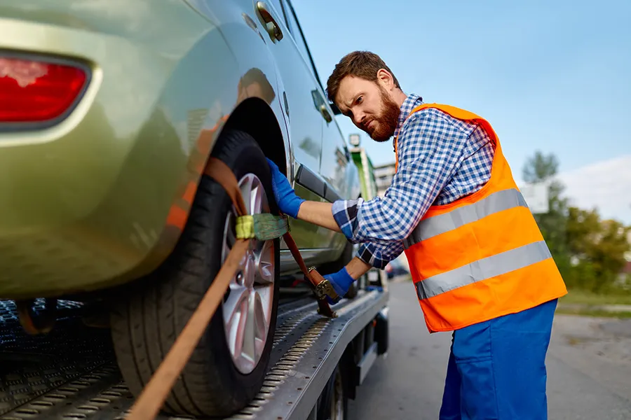 Tow truck operator securing a vehicle to a flatbed tow truck — representing SEO for towing companies targeting emergency roadside assistance, vehicle recovery, and scheduled automobile transport services.